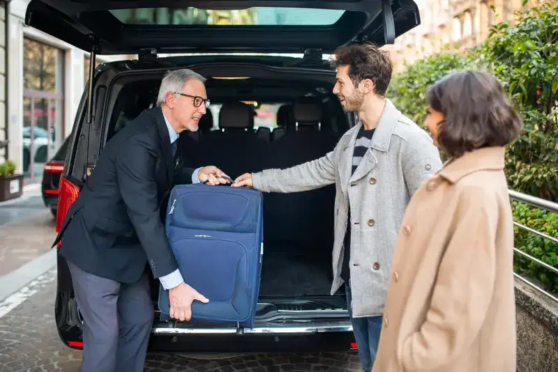 A Black Car Service Private Chauffeur helping a couple with their luggage after they arrived to their destination. Symbolizing IAH airport black car service.